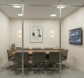Un salón de conferencias con una larga mesa, cuatro sillas, una pantalla de proyector mostrando gráficos y dos lámparas fijadas a la pared.