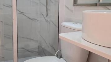 Een badkamer met een douchecabine van glas, een toilet en een wastafel met spiegel erboven.
