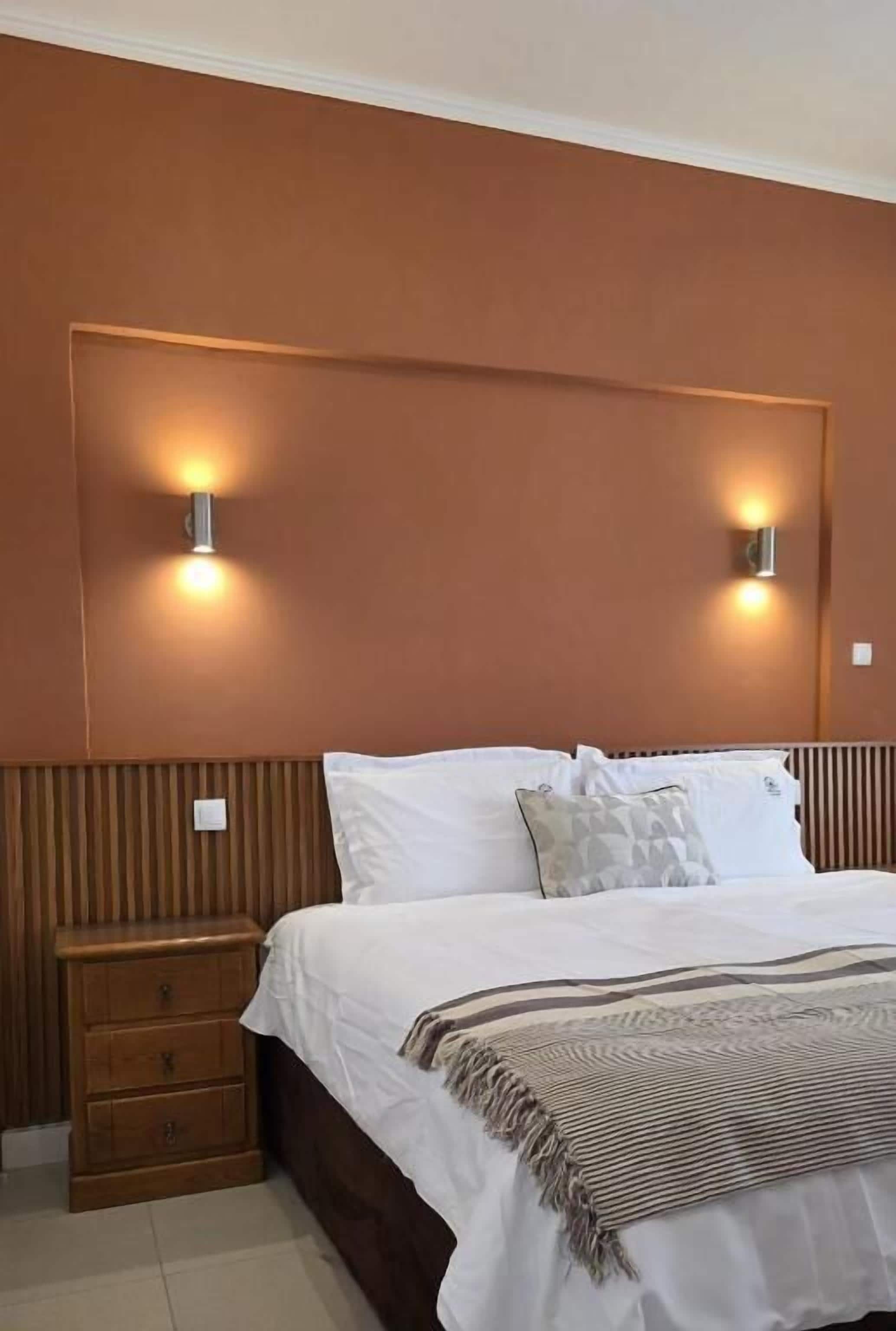 Un dormitorio con cama, mesitas de noche e iluminación en la pared.