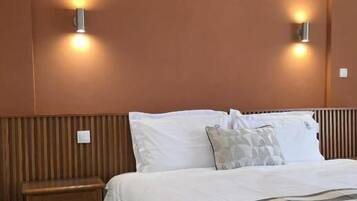 Un dormitorio con cama, mesitas de noche e iluminación en la pared.
