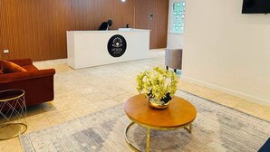 A hotel reception area with a reception desk, a sofa, a coffee table, and a decorative plant. - Pérola Suítes Boutique Hotel (Luanda)