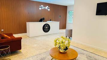 Een hotel receptie met een receptiebalie, een bank, een bijzettafeltje en een sierplant.