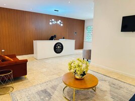 Uma área de recepção de hotel com balcão, sofá, mesa de centro e planta decorativa.