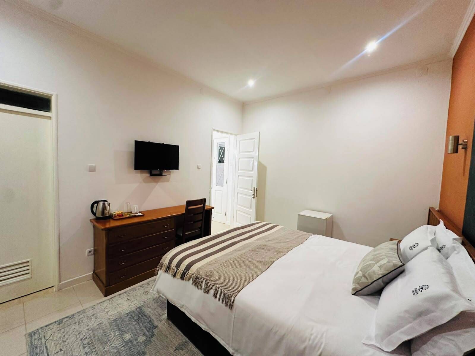 Un dormitorio con cama, cómoda, televisor y puerta.