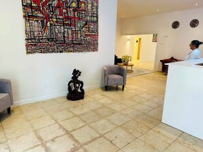 Uma área de recepção com uma grande pintura abstrata, uma escultura, uma poltrona cinza e um balcão de recepção.