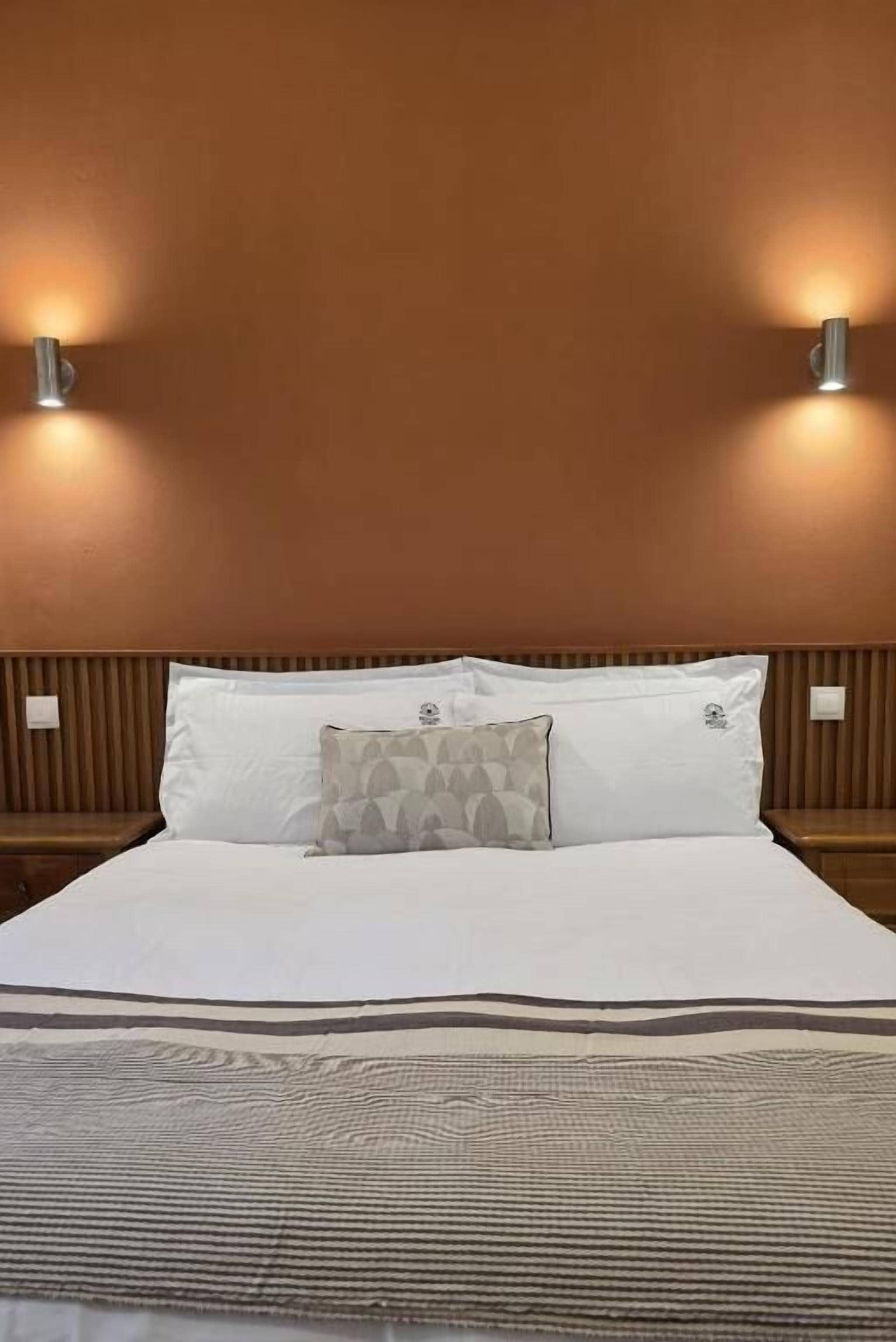 A hotel room with a bed, two wall-mounted light fixtures, and a patterned throw blanket.