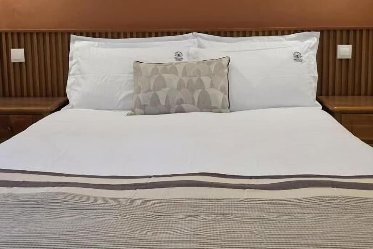 A hotel room with a bed, two wall-mounted light fixtures, and a patterned throw blanket.