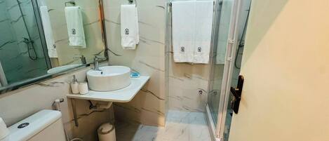A bathroom with a toilet, sink, mirror, and shower area.