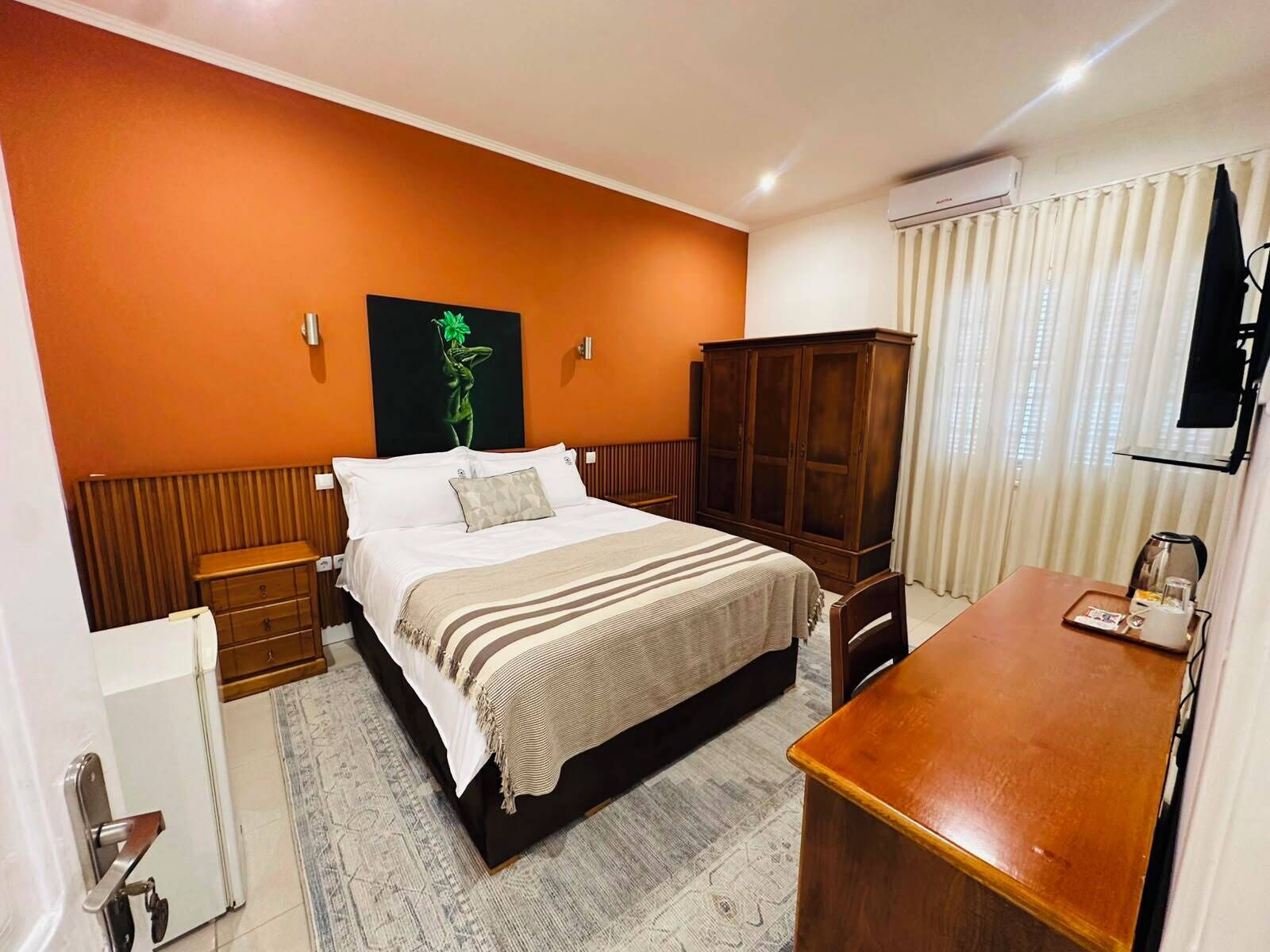 A hotel room with a bed, a wooden cabinet, a desk, and a radiator.