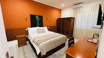 A hotel room with a bed, a wooden cabinet, a desk, and a radiator.