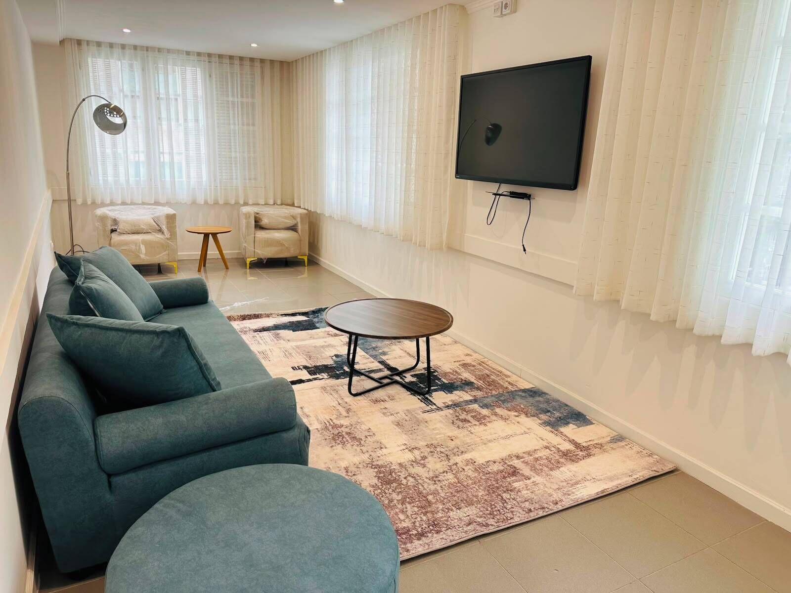 Una sala de estar con un sofá modular, una mesa de centro, un televisor montado en la pared y una alfombra estampada.