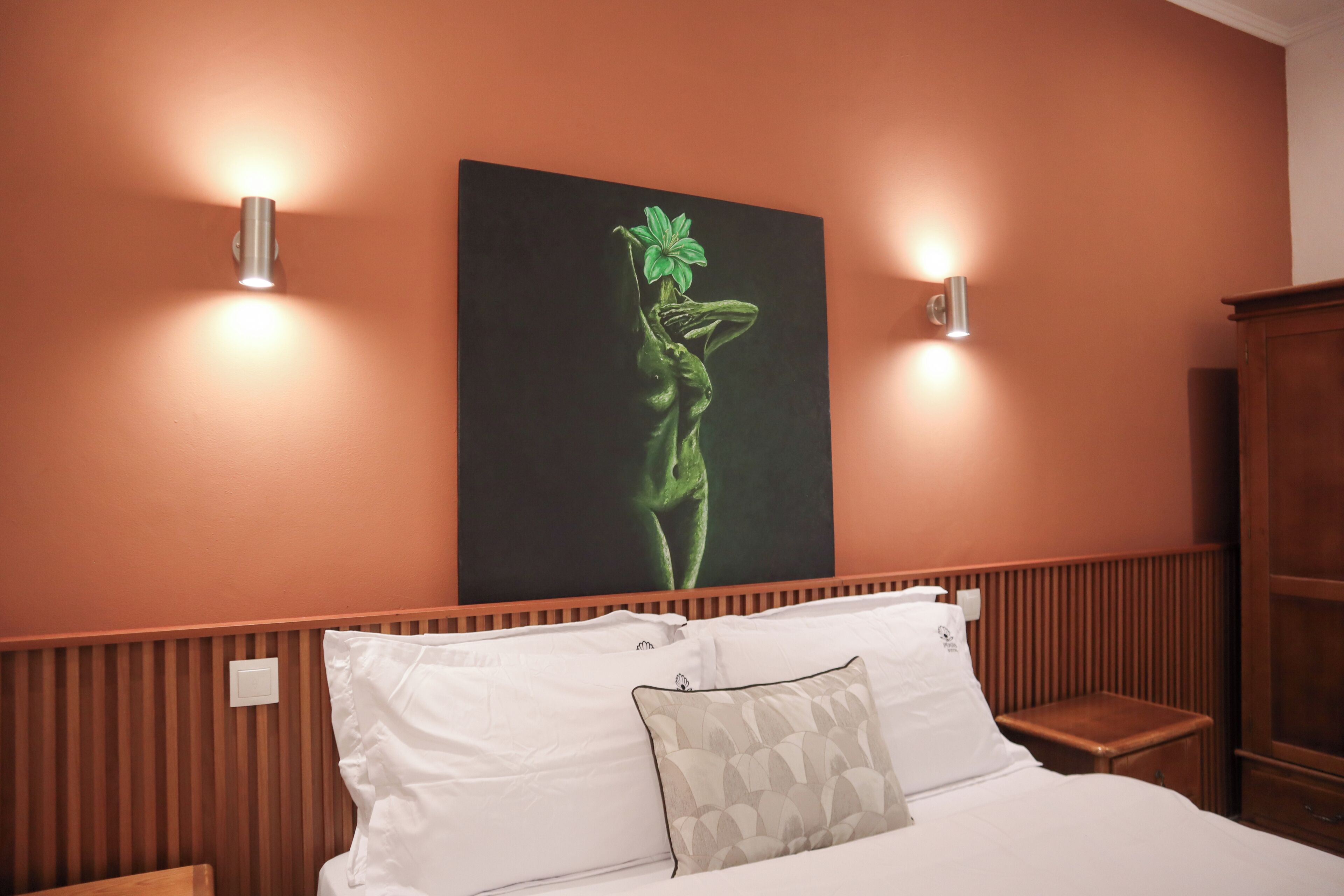 A hotel room with a bed, two wall-mounted lights, and a large painting on the wall.