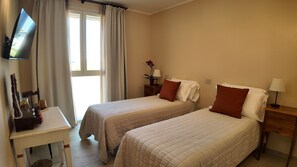 Ett hotellrum med två sängar, ett skrivbord, en tv och ett fönster med gardiner.