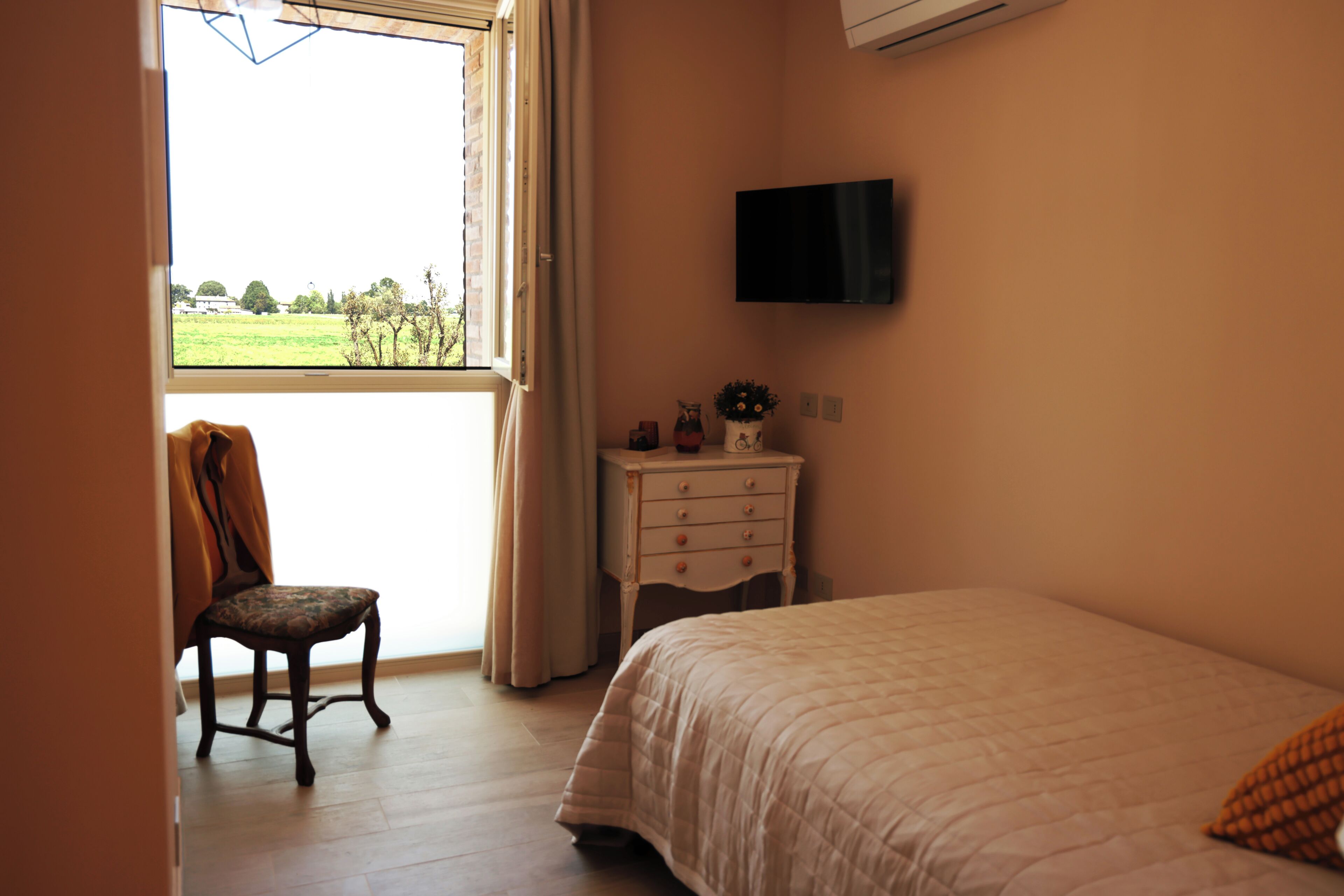 Un dormitorio con cama, una silla, cómoda y televisor en la pared.