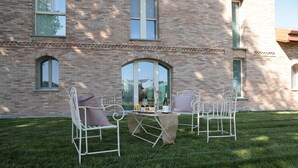 An outdoor seating area with metal chairs and a table, set against a brick building with large windows. - Agriturismo Ca' Brusca (Reggio nell'Emilia)