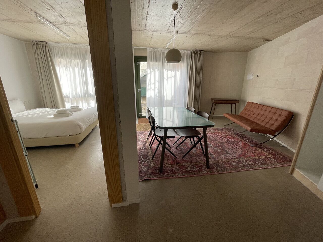 Ein Zimmer mit einem Bett, einem Esstisch mit Stühlen, einer Bank und einem gemusterten Teppich.