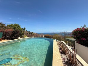 Ein Pool mit klarem Wasser und Blick auf das Meer und die Hügel.