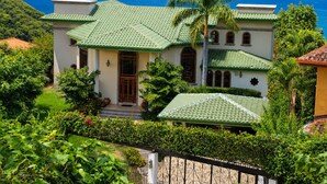 A two-story house with a green roof, surrounded by lush greenery and a view of the ocean. - Oceanview Luxury Villa in Playa Hermosa | 4 BR - 4.5 Baths & Private Pool (Playa Hermosa)