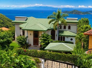 Ein zweistöckiges Haus mit grüner Dachbegrünung, umgeben von üppiger Vegetation und Blick auf das Meer.