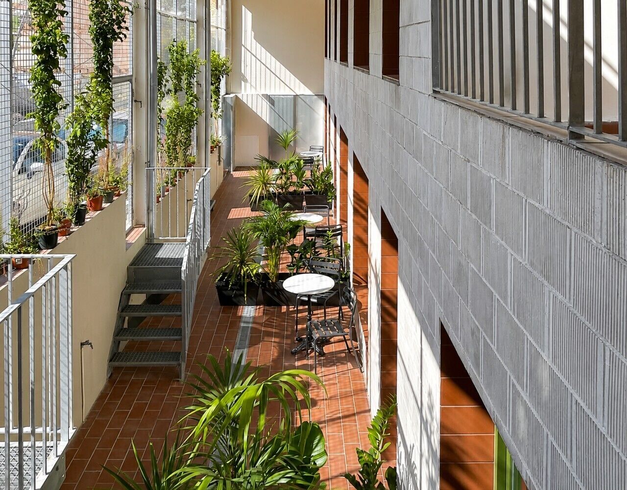 Een meerlaags atrium met een centrale binnenplaats, buitenmeubilair, potplanten en een trap.