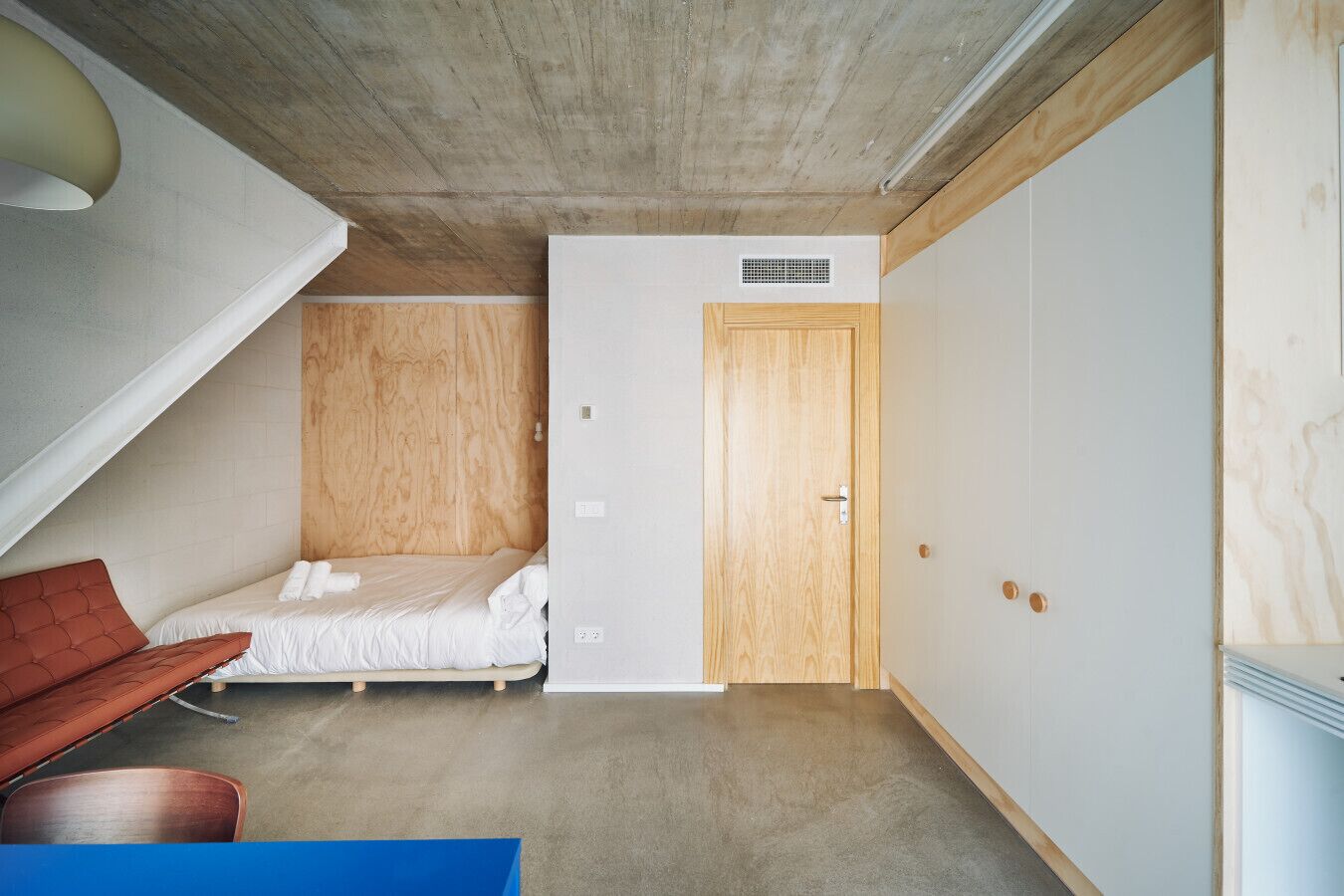 A compact room with a loft bed, a small seating area, and a wardrobe.