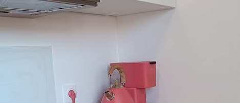A kitchen with a wooden countertop, a pink kettle, and a white oven.