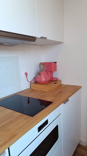 A kitchen with a wooden countertop, a pink kettle, and a white oven. - defaultName (Songeons)