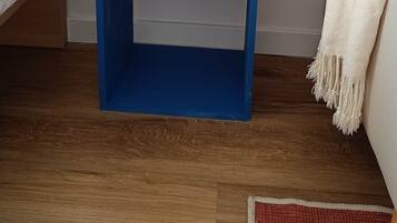 Een blauwe boekenkast met boeken en een afstandsbediening, een witte plant en een witte plaid op een houten vloer.