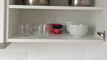 A kitchen with stainless steel cookware on shelves, clear drinking glasses, a red electric kettle, and a white mixing bowl.
