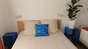 A bed with a headboard, two pillows, a bedside table, a nightstand, and a potted plant. - defaultName (Songeons)