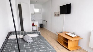 A bedroom with a bed, a TV, a wooden side table, and a hallway leading to a bathroom.