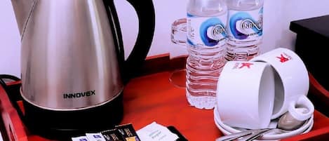 A tray with a stainless steel INNOVEX kettle, two bottles of Infinity water, a white mug with a spoon, and several travel cards.