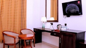 A hotel room with a desk, two chairs, a lamp, a television, and a mirror.