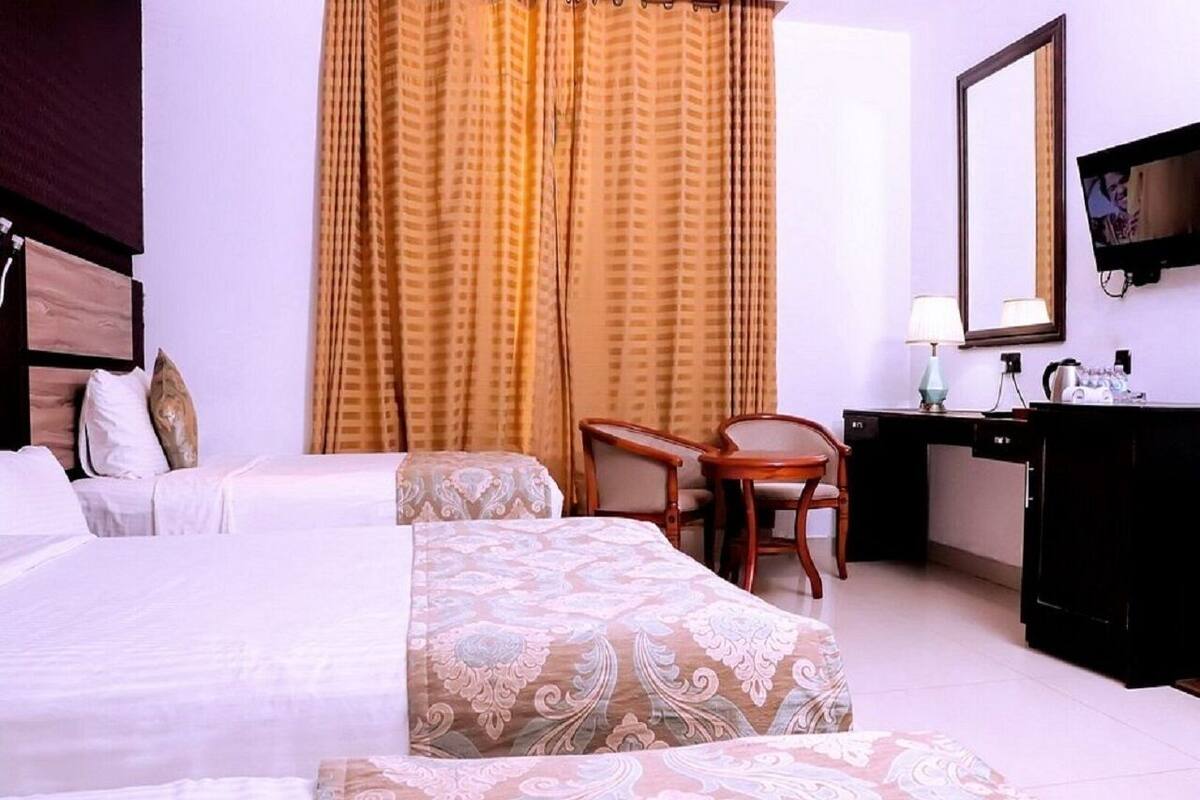 A hotel room with two beds, a desk, a chair, a dresser, and a television.