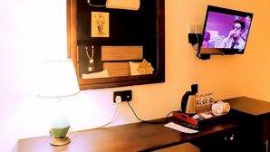 A hotel room with a bed, a TV mounted on the wall, a lamp, and a small table with a remote control and a cup.