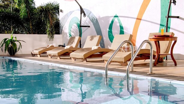 A swimming pool with lounge chairs and a table, surrounded by greenery and a colorful mural.