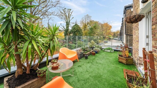 Eine Terrasse mit Kunstgrasanlage, orangenen Sitzmöbeln und Kübelpflanzen.