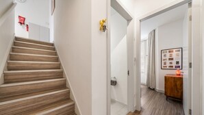 Eine Treppe führt zu einem Flur mit Holzboden, einer Tür, an der ein Handtuch hängt, und einem gerahmten Foto an der Wand.