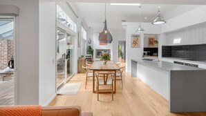 Cozinha moderna com ilha central, iluminação pendente e área de refeições com mesa e cadeiras de madeira.