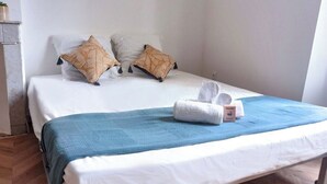 Ein Bett mit weißer Bettwäsche, zwei gemusterte Kissen, einer blauen Decke und einem zusammengerollten Handtuch mit einer Willkommenskarte.