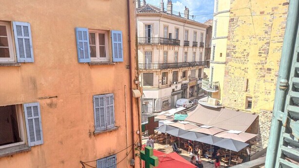 Eine enge Straße mit Häusern, ein Café mit Außenbestuhlung und einer sichtbaren Treppe.