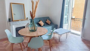 Ein Essbereich mit einem runden Tisch, Stühlen, einer Vase mit Trockenpflanzen, einer Couch mit Kissen und einem Kamin.