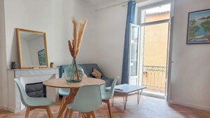 Ein Essbereich mit rundem Tisch, Stühlen, einer Vase mit Pampasgras, einer Couch und einem Balkon mit Geländer.