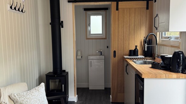 A compact living space with a kitchenette, a sofa, a fireplace, and a small window. - Woodland get away 0.7 mile walk from the beach ! (Mawgan Porth)