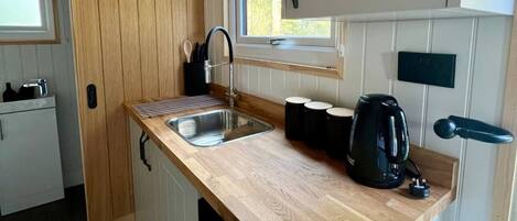 A compact kitchen with a wooden countertop, a sink, and a kettle.