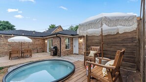 Un jardin avec une piscine, une terrasse en bois, du mobilier d’extérieur et une maison en briques.