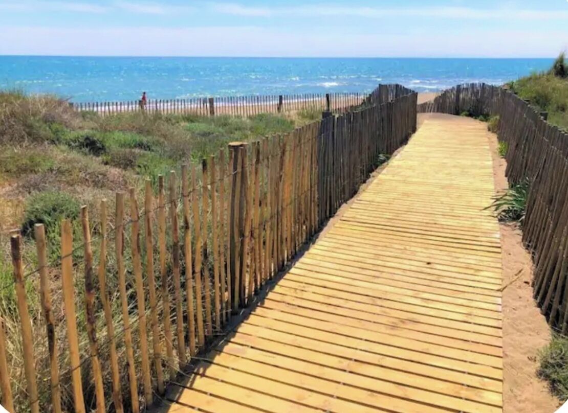 Una pasarela de madera que conduce a una playa, con una valla a un lado.