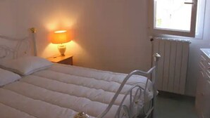 Un dormitorio con cama, lámpara de noche, radiador y ventana.