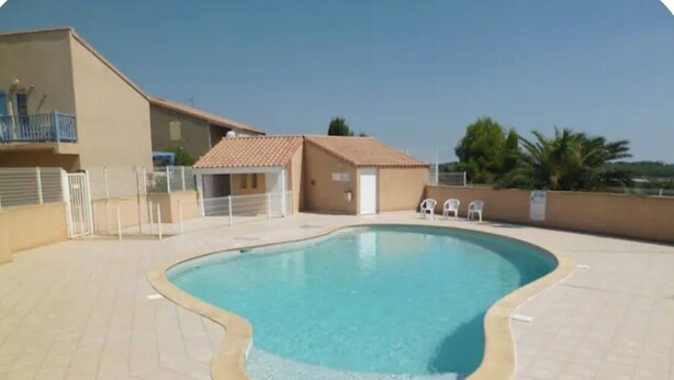 Una piscina con solárium empedrado, un edificio pequeño y algunas sillas.