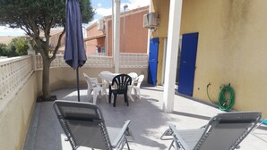 Un patio con mobiliario exterior, una puerta azul y un equipo de aire acondicionado.
